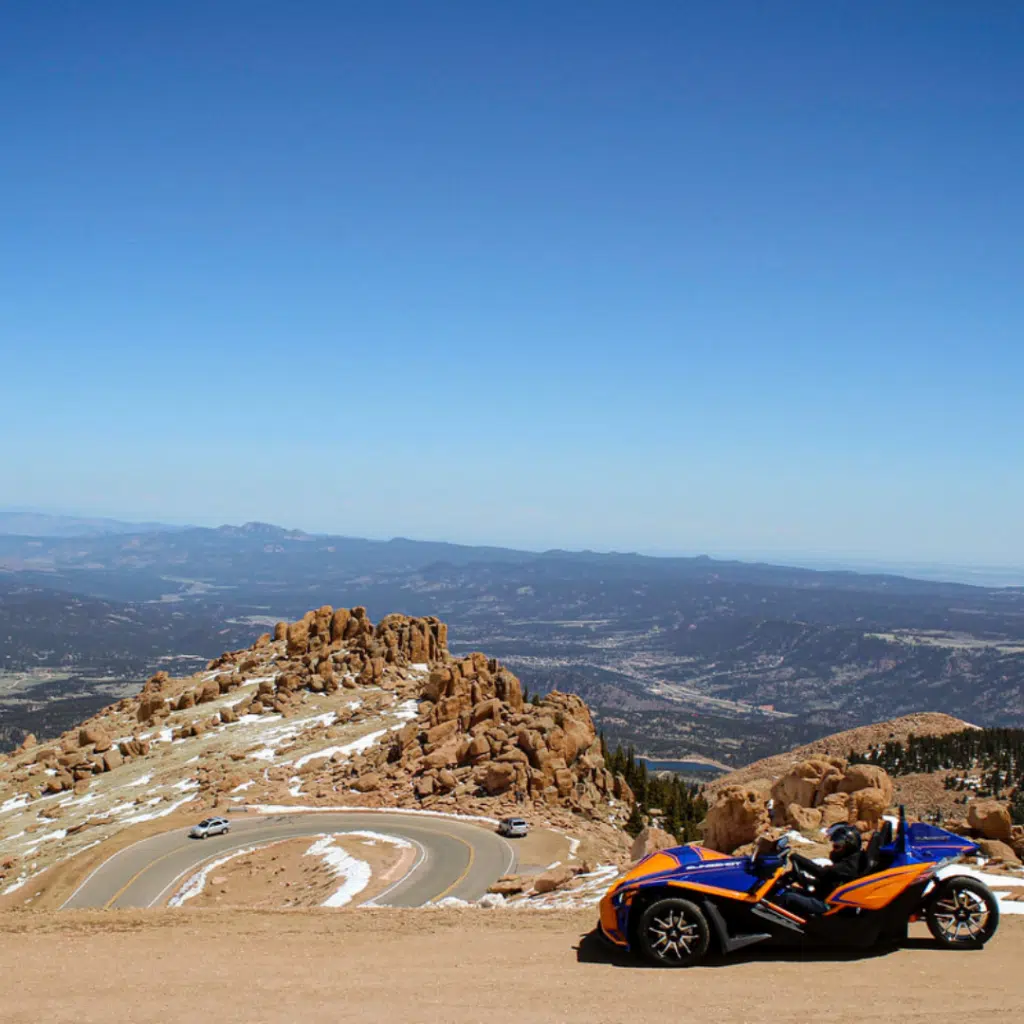 Sunrise orange Polaris slingshot at the top of a rocky Colorado mountain