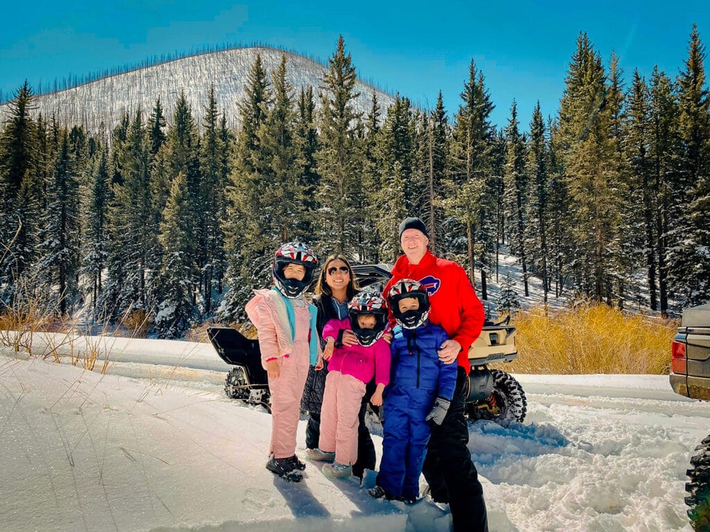 Familia vestida con ropa de nieve de invierno disfrutando de un tour en UTV cerca de Woodland Park, Colorado, manteniéndose abrigados y seguros durante las aventuras invernales todoterreno con Great Outdoors Adventures.