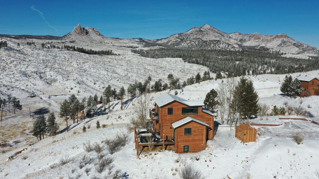 Acogedoras cabañas de troncos en Pikes Peak Ranch, cerca de Woodland Park, con un paisaje invernal de montaña cubierto de nieve al fondo.