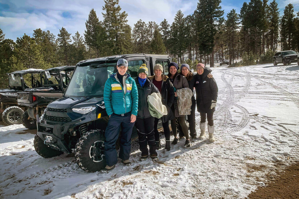 Group of women posing outside an enclosed 6-seater Polaris Ranger UTV rental on a snow-covered trailhead in Colorado