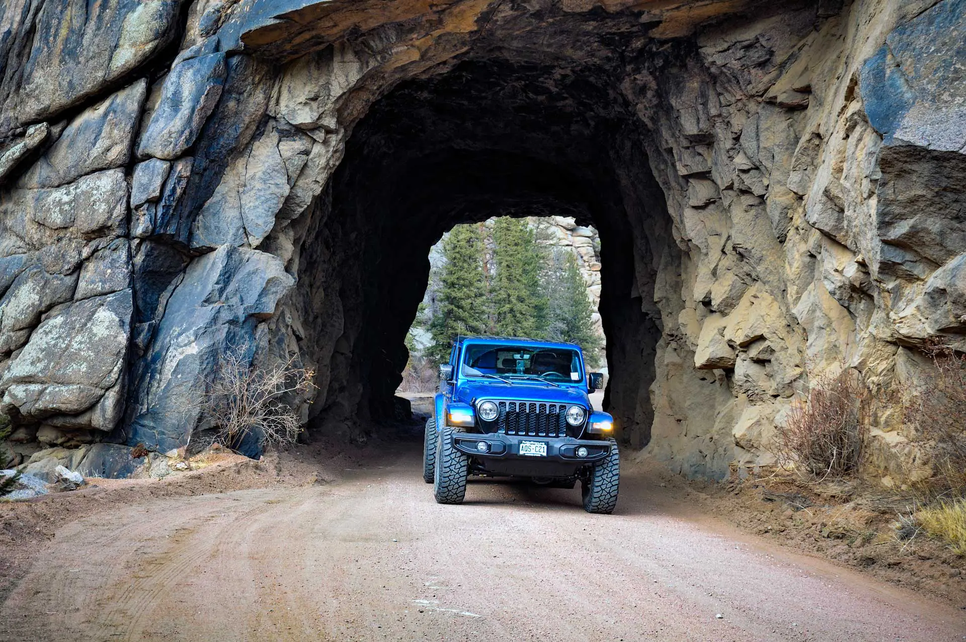 Blue Jeep Gladiator 4x4 rental driving through a mountain rock tunnel near Woodland Park, Colorado
