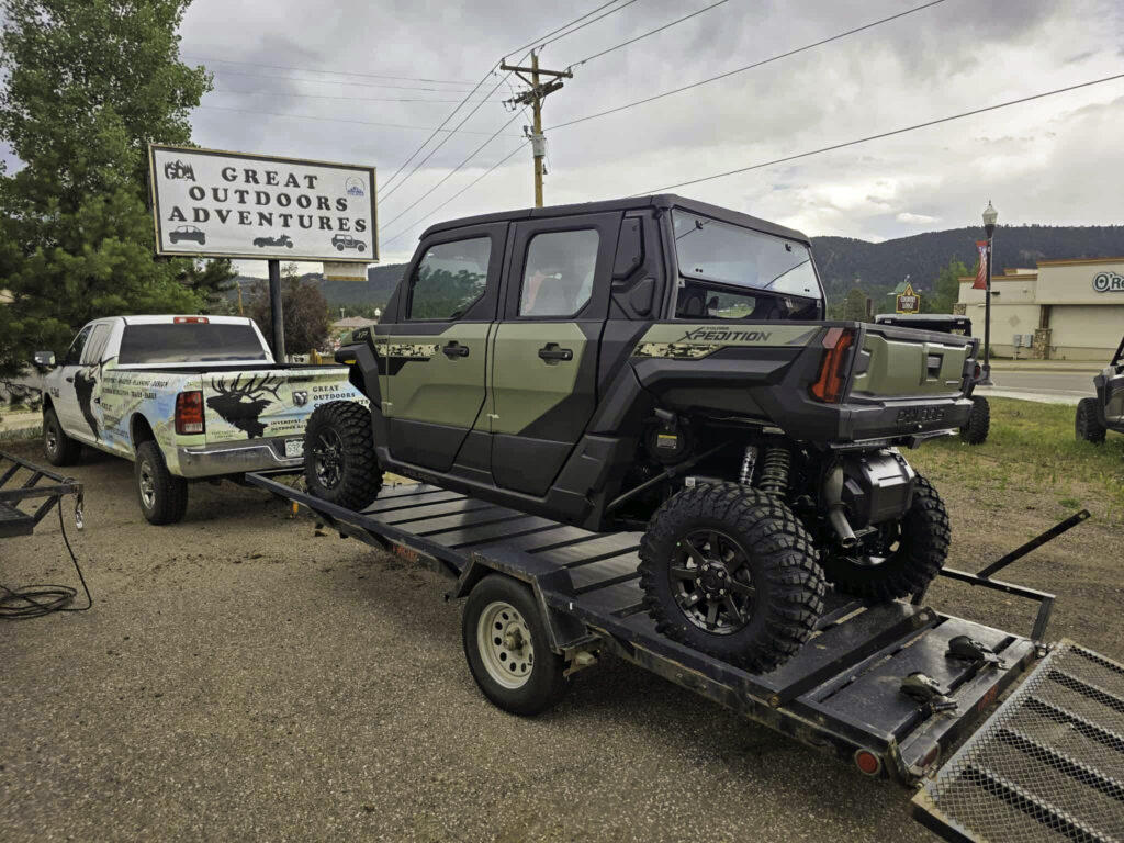 Enclosed green Polaris Expedition UTV loaded on a transport trailer outside the Great Outdoors Adventures sign in Woodland Park Colorado
