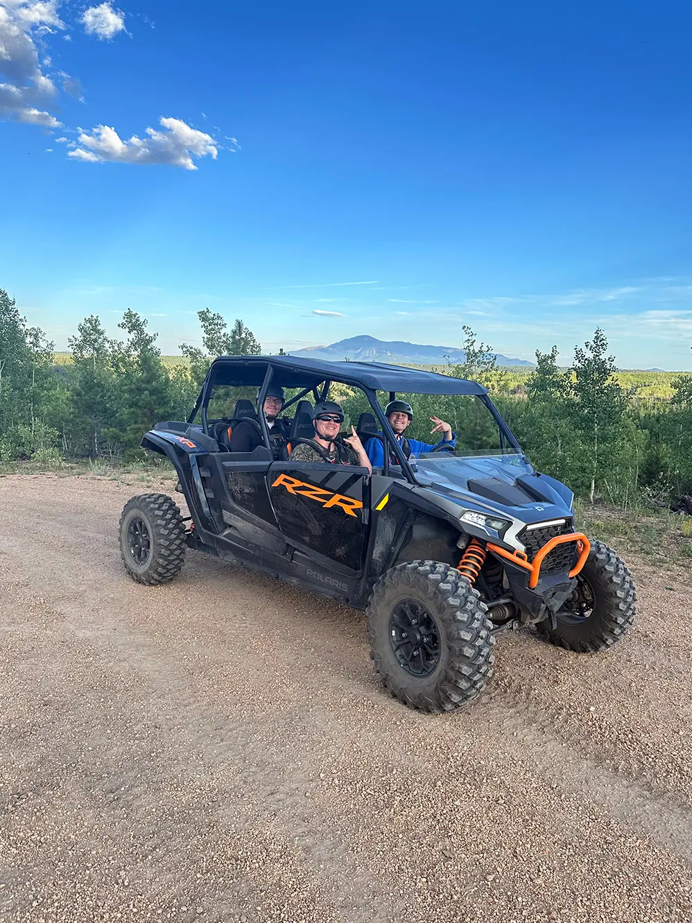 Happy group riding a Polaris RZR UTV on a scenic trail with Pikes Peak in the background near Woodland Park, Colorado