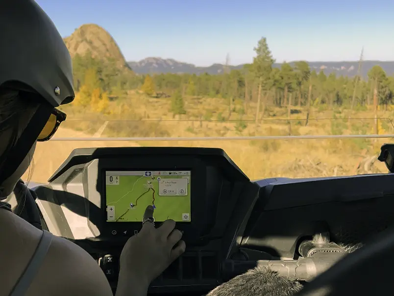 Driver wearing a helmet using a digital GPS navigation screen inside a Polaris UTV while riding on scenic Colorado mountain trails during fall.